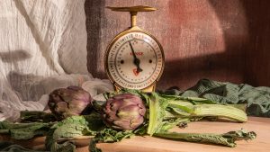 Artichokes and scale sit on a wooden table.
